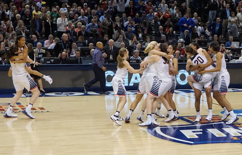 Jugadores de básquetbol universitario de la NCAA disputan un balón durante un partido de exhibición en un estadio.